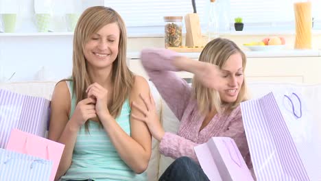 Delighted-woman-giving-her-girlfriend-a-present-sitting-between-shopping-bags