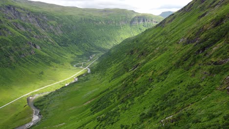 deep lush green valley of vikafjell and myrkdalen with sun patches on road in bottom - beautiful aerial moving downwards along steep mountainside - norway