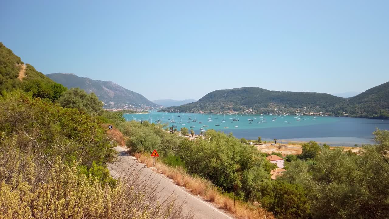Bay of blue water with sail boats surrounded by green mountains, static