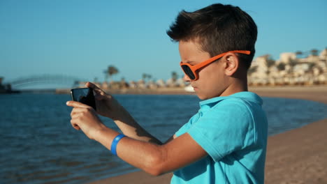 Attractive-teenage-boy-taking-pictures-by-mobile-phone-at-sunny-coastline.