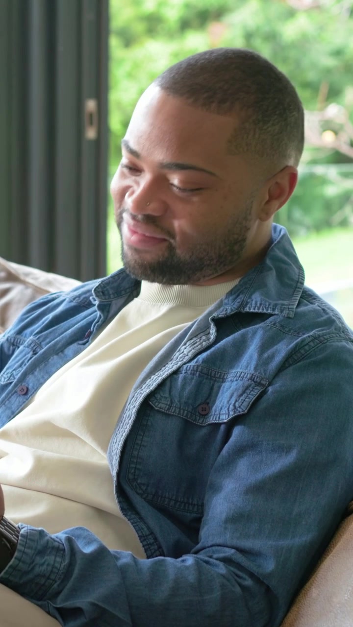 Vertical video: Checking phone, man in denim looking out, reflecting, returning to screen at home