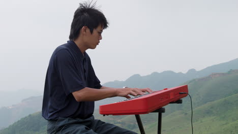 Young-asian-man-concentrating-on-playing-the-piano-on-a-hilltop-on-a-windy-day