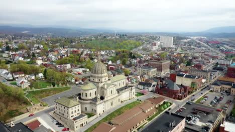Aerial-drone-flying-over-small,-rural-downtown-of-Altoona-Pennsylvania-in-the-summer-showcasing-the-buildings-and-large-church