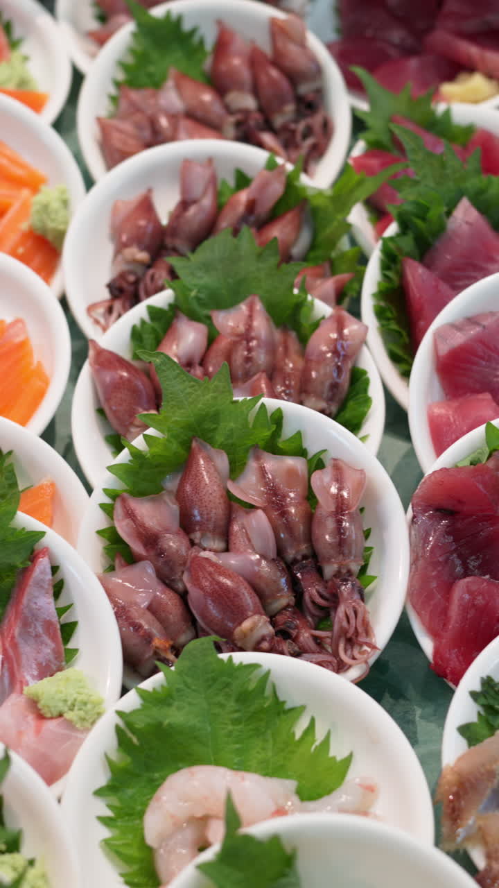 Close up of different seafood in small white bowls on display at the Tsukiji Fish Market in Japan. Vertical