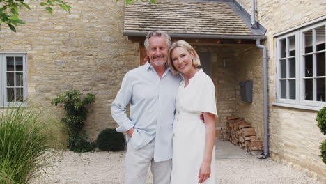 Portrait-Of-Loving-Senior-Couple-Standing-Outside-Front-Door-Of-Home