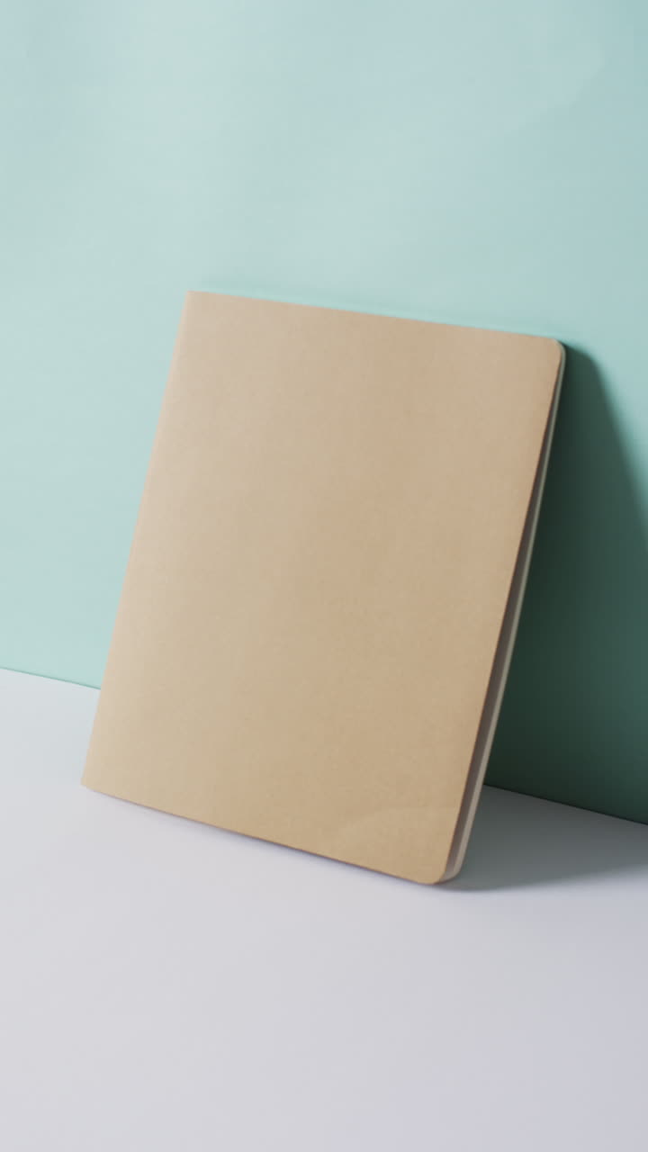 Vertical video of closed beige book leaning on wall with copy space in slow motion
