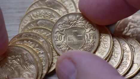 mano masculina inspeccionando un montón de monedas doradas de veinte francos iluminadas en el estudio, primer plano