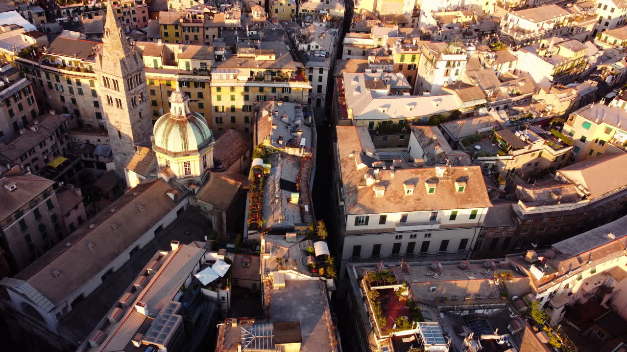 Drone pans over Genoa’s historical center, tilts down to a full top-down view of rooftops with dome and tower visible at sunset
