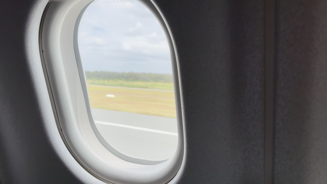 Aircraft moves along runway, exterior landscape visible through window, natural daylight, steady interior perspective