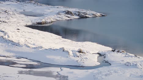 the first snow covers the banks of the small lake