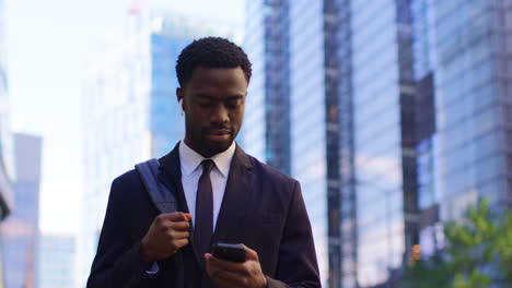 young businessman wearing wireless earbuds streaming music or podcast from mobile phone walking to work in offices in the financial district of the city of london uk 1