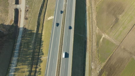 Sonnenlicht-Tanzt-über-Eine-Autobahn-Und-Wirft-Lange-Schatten-Von-Einer-Reihe-Vorbeifahrender-Fahrzeuge-Vor-Einer-Ländlichen-Landschaft