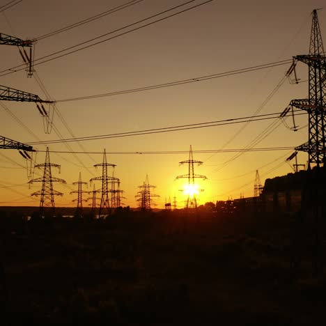 dark silhouette of transmission towers at sunset. high-voltage electric lines against the orange setting sun. electricity distribution.