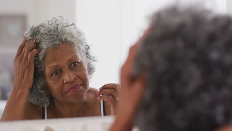 Ältere-Afroamerikanische-Frau-Berührt-Ihr-Haar,-Während-Sie-Zu-Hause-In-Den-Spiegel-Schaut