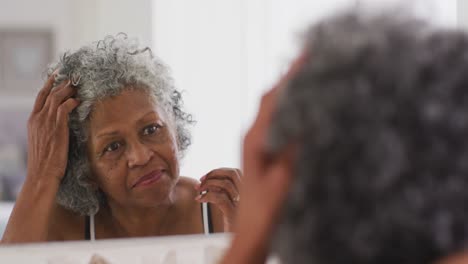 mujer afroamericana mayor tocando su cabello mientras se mira en el espejo en casa
