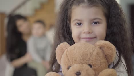 close-up face of a happy middle eastern girl with brown eyes and curly hair holding the teddy bear and smiling