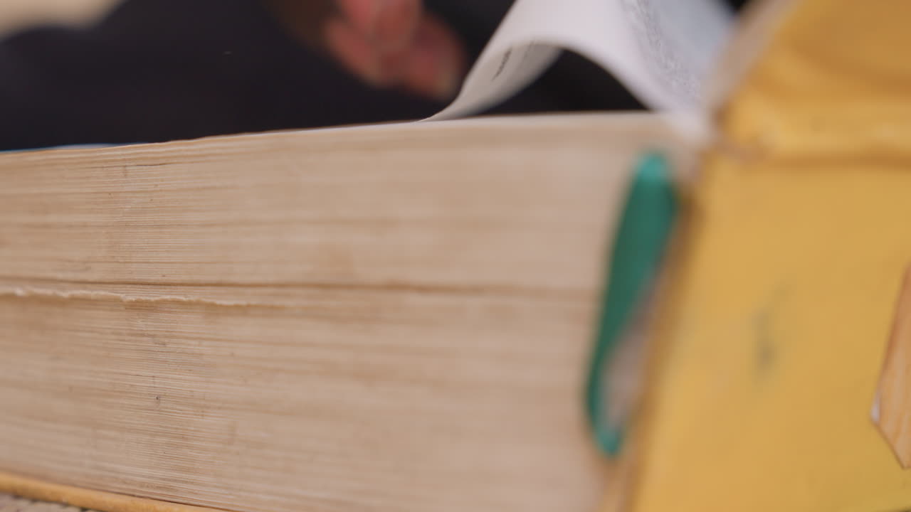 Sorte hænder bladrer i slidte paperback-sider i nærbillede, tommelfinger vender gulnet papir, tekstureret ryg med grønt bogmærke, stille studiemoment for sort studerende forsker, intimt taktilt fokus, varmt.