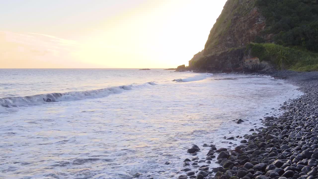 Sudut pandang rendah deburan ombak di pesisir berbatu di pulau Hawaii, Maui saat matahari terbenam