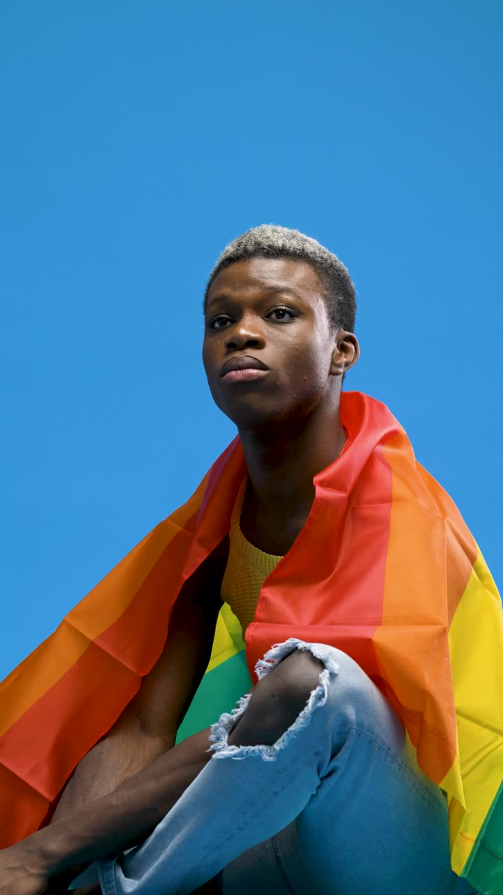 Giovane persona di colore avvolta in una bandiera arcobaleno del Pride