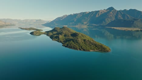 Lush-green-island-in-calm-alpine-Wakatipu-lake-of-New-Zealand,-aerial-view