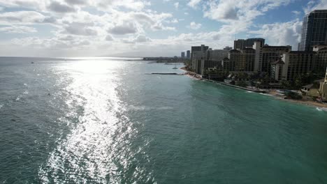 a drone glides towards the sun at a tropical beach location with luxury hotels and families on vacation