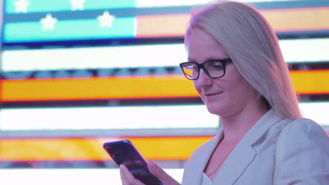 business woman uses a smartphone on the background of a large american flag on the famous times squa