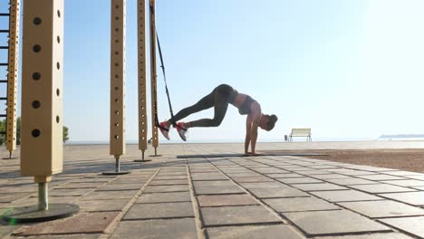 entrenamiento al aire libre. correas de suspensión. entrenamiento con correas. mujer joven atlética está haciendo ejercicios de resistencia de todo el cuerpo usando cuerdas en bucle trx, en la playa durante la puesta o el amanecer. entrenamiento de fitness al aire abierto. concepto de estilo de vida saludable. deporte matutino