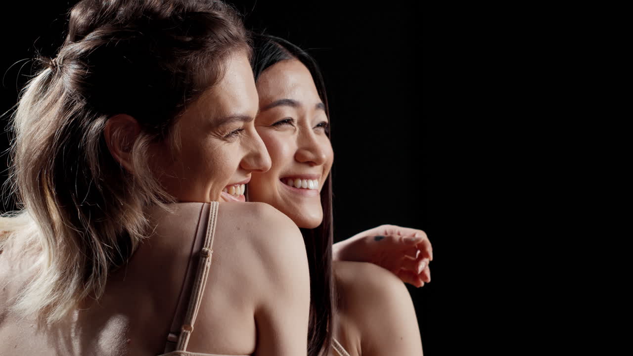 Two smiling women embracing against a black background