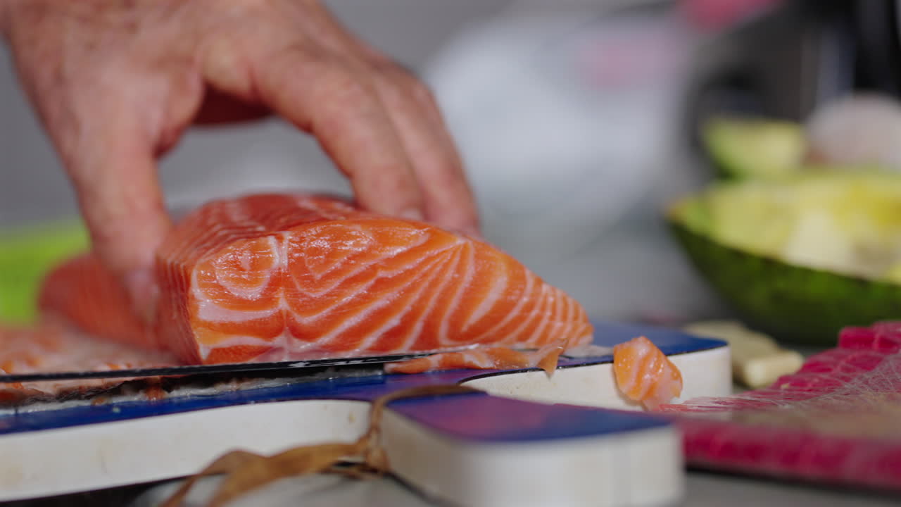 Close-up of a chef cutting fresh salmon off its skin with a sharp knife, preparing for sushi