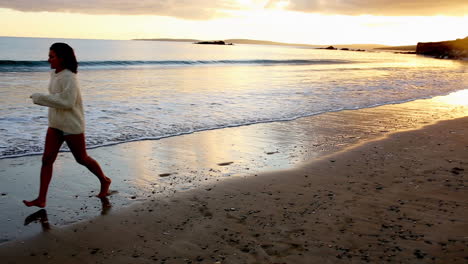 Woman-skipping-along-the-water-at-sunset