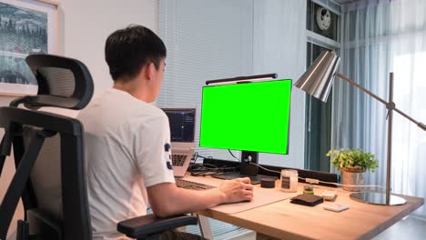 현대 가정 사무실 에서 나무 책상 에서 녹색 화면 디스플레이 컴퓨터 로 일 하는 아시아인