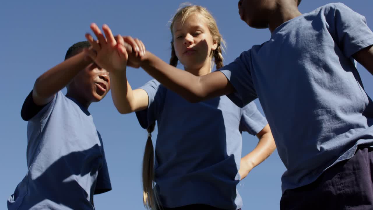 Bambini diversi con magliette blu che impilano, toccano le mani quando una bambina controlla il palmo, esultando al parco