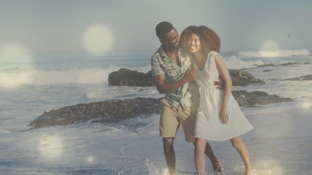 Uomo che accarezza il viso di una donna, coppia che cammina sulla battigia, onde che si infrangono, bokeh che mostra romanticismo per i viaggi.