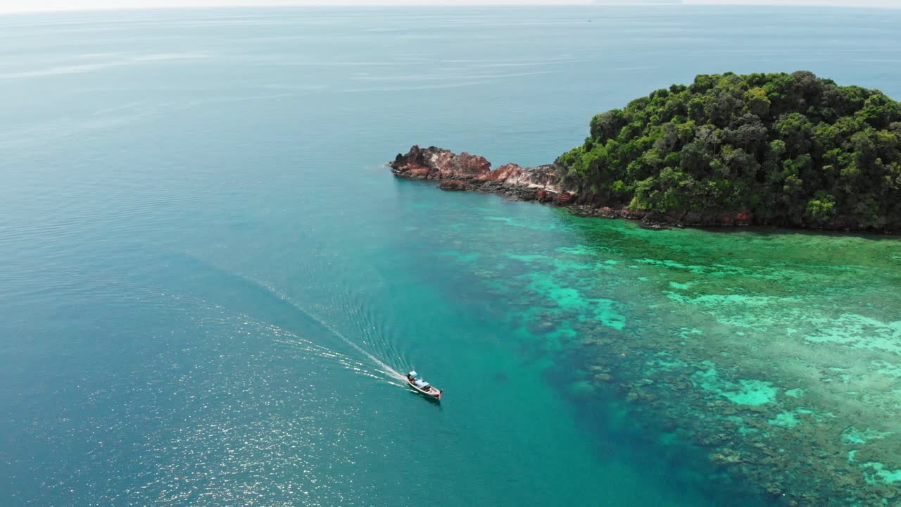 An aerial footage of a boat driving past a stunning island in Thailand