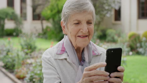 retrato de una mujer mayor feliz usando un teléfono inteligente sonriendo disfrutando de ver medios en el teléfono móvil en un hermoso fondo de jardín
