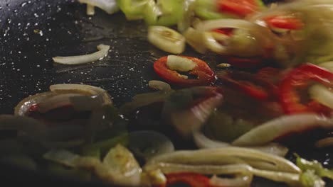 an extremely detailed close up of colorful, sizzling, oiled sliced onions and peppers in a skillet and then stirred with a wooden spatula