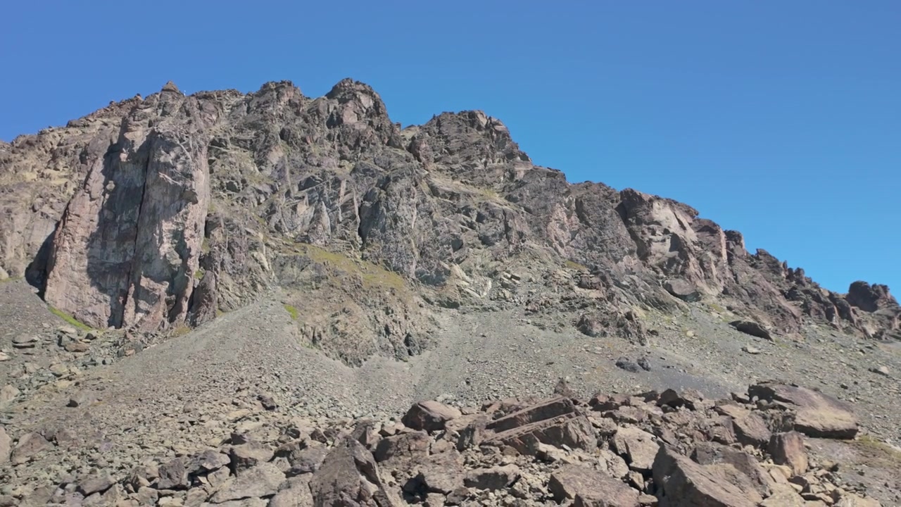 Cresta montuosa vulcanica aspra con roccia affiorante, ghiaione sciolto e un cielo azzurro limpido in un paesaggio alpino desolato della Silvretta. Movimento a destra.