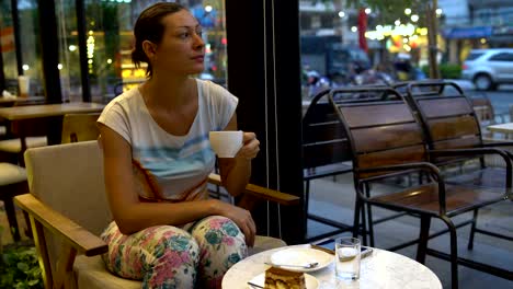 a woman sits at a coffee shop at a table and drinks coffee