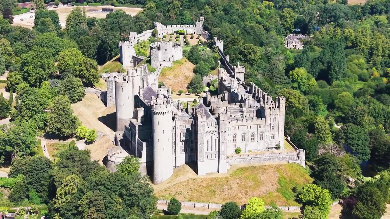 Orbita aerea del Castello di Arundel che si inverte mentre il drone si allontana dalla fortezza e dalle torri medievali, rivelando un parco collinare boscoso nel West Sussex, Inghilterra, in una luminosa giornata estiva.