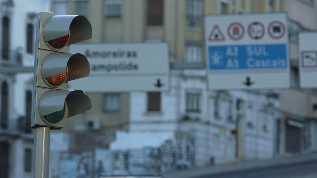 Green, Red, And Yellow Traffic Lights Changing At The Marques De Pombal Roundabout In Lisbon, Portugal With Blurry Road Signs In The Background - Closeup Side Shot
