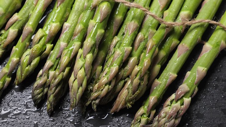 Raw green asparagus on wet black slate background