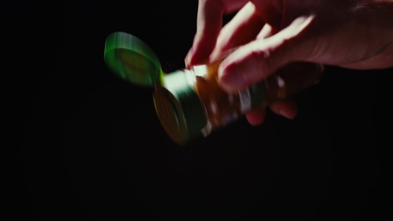Chef's hand elegantly sprinkling Paprika powder against a black background. Slow motion shot with professional studio lighting