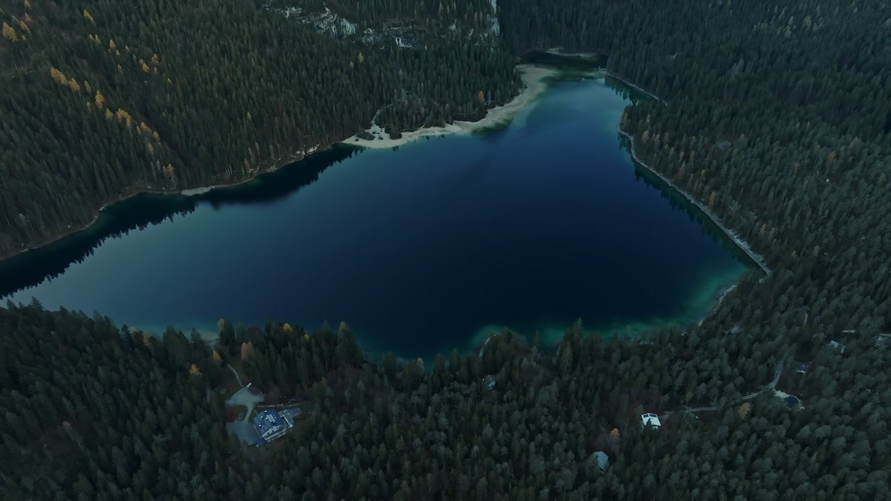 Vista drone su una fitta foresta di pini che rivela un lago alpino blu, stagione invernale, prima mattina.