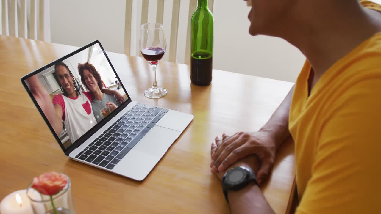 Mid section of african american man with wine while having a video call on laptop at home