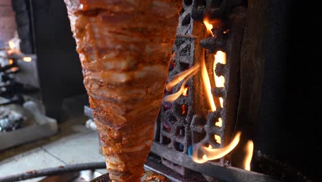 al pastor meat cooking on vertical spit with open flame