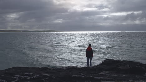 Woman-Looks-Out-At-Sea-Under-Ominous-Clouds-Pre-Storm-on-Isle-of-Barra-Scotland-4K