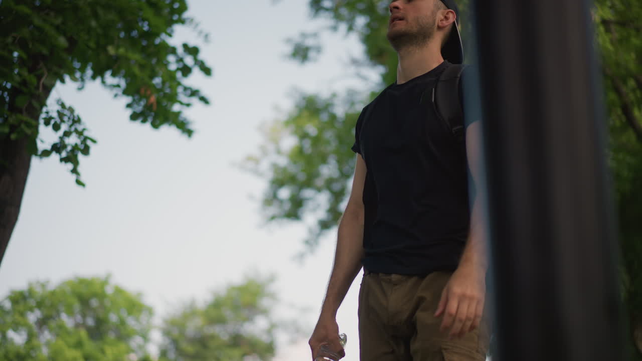 Traveler Refreshes By Drinking Water In Sunlight, Hiker Takes Hydration Break Beside Tree In Sun, Wayfarer Replenishes Liquids And Relaxes In Shade Of Tree During Sunny Outdoor Trek
