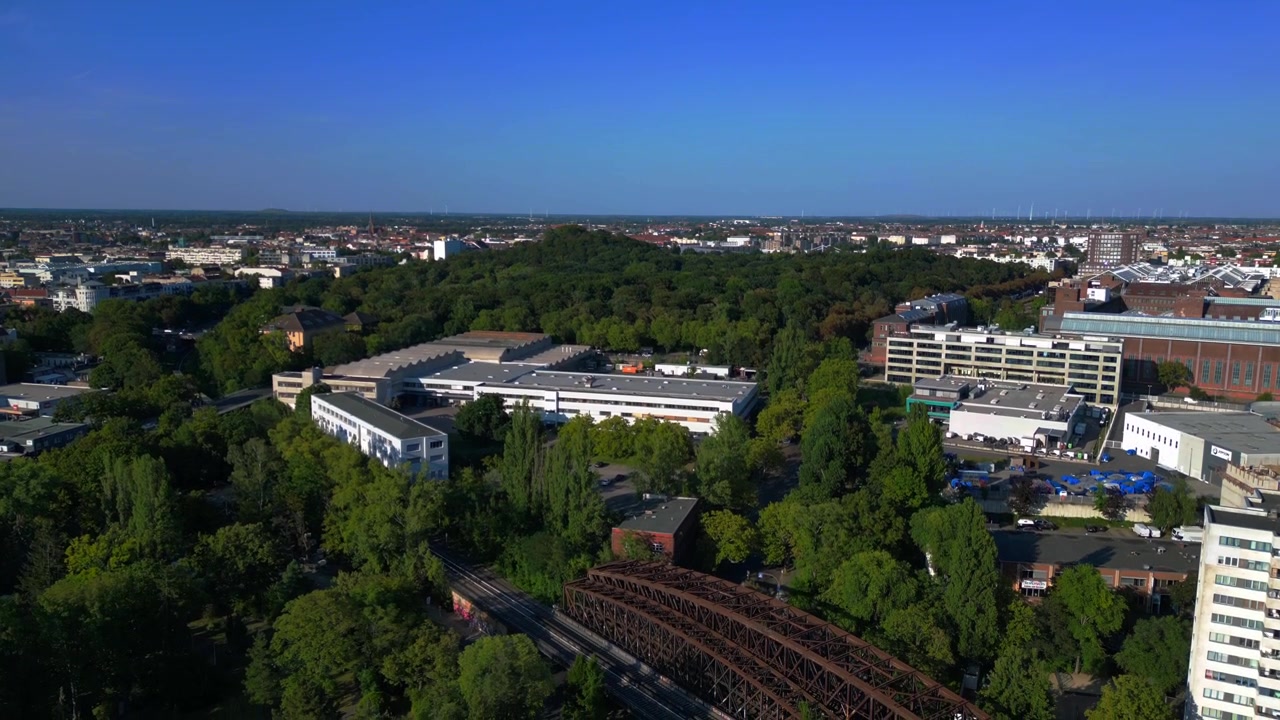 Ponte ferroviária enferrujada passando sobre trilhos de trem em um cenário urbano verde exuberante em Berlim, Alemanha, infraestrutura de transporte. Voo de drone com vista aérea inacreditável em descida.