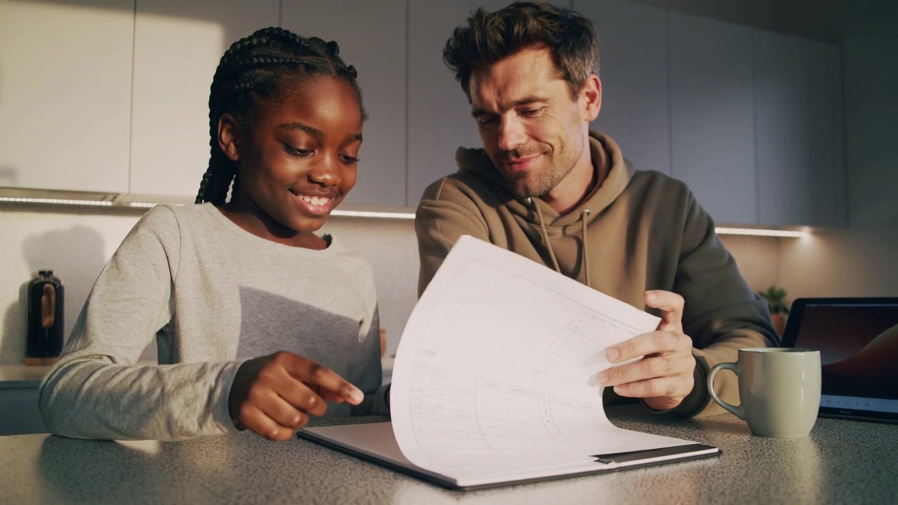 Pointing school-age girl guiding adult in tan hoodie through homework at kitchen counter, clipboard