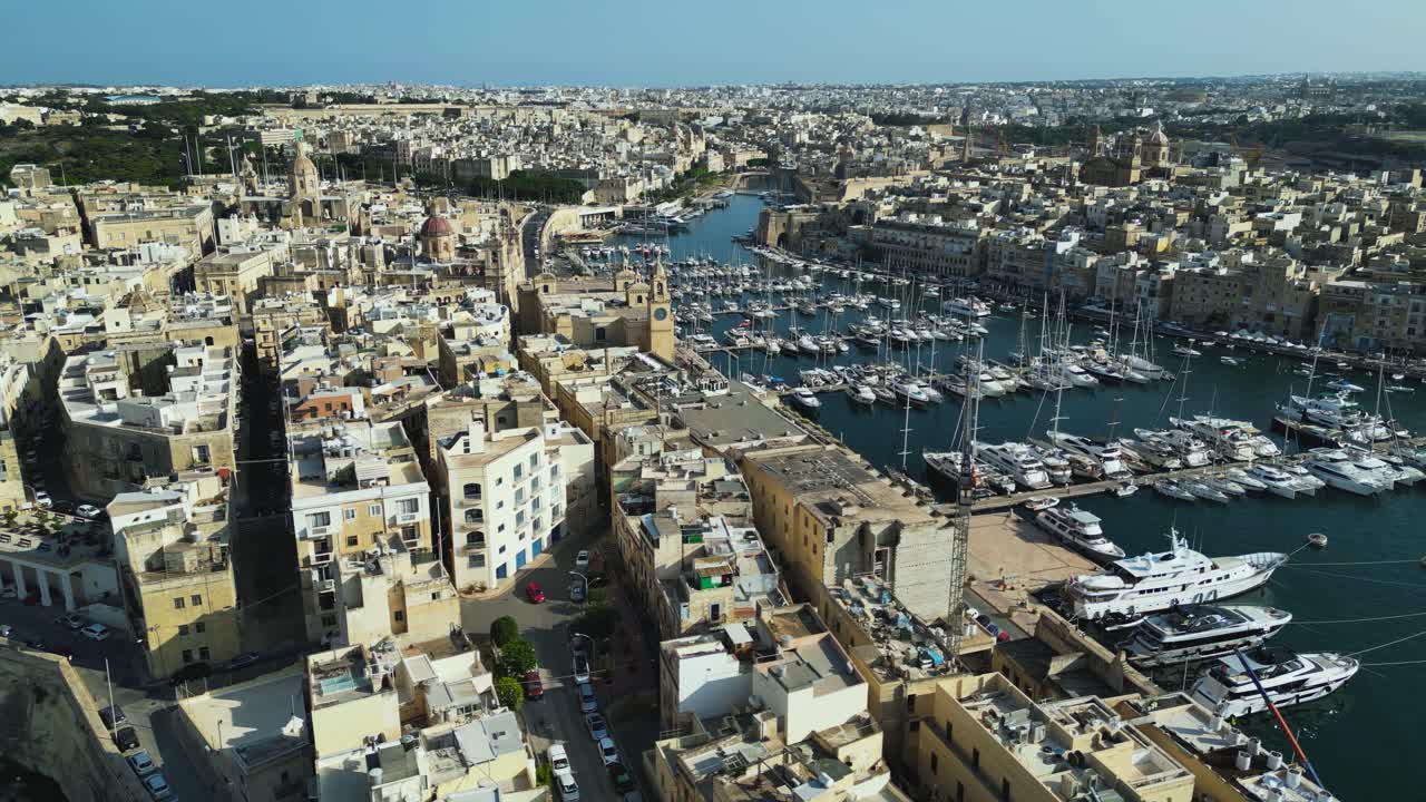 Panoramica aerea del porto di Birgu e degli edifici in pietra, dei moli del porto turistico e delle acque cristalline del Mediterraneo a mezzogiorno, Malta